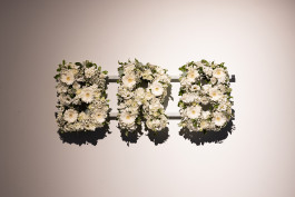 An arrangement of white funeral letters made of a variety of white flowers. The letters spell the initialism BRB: Be right back. 